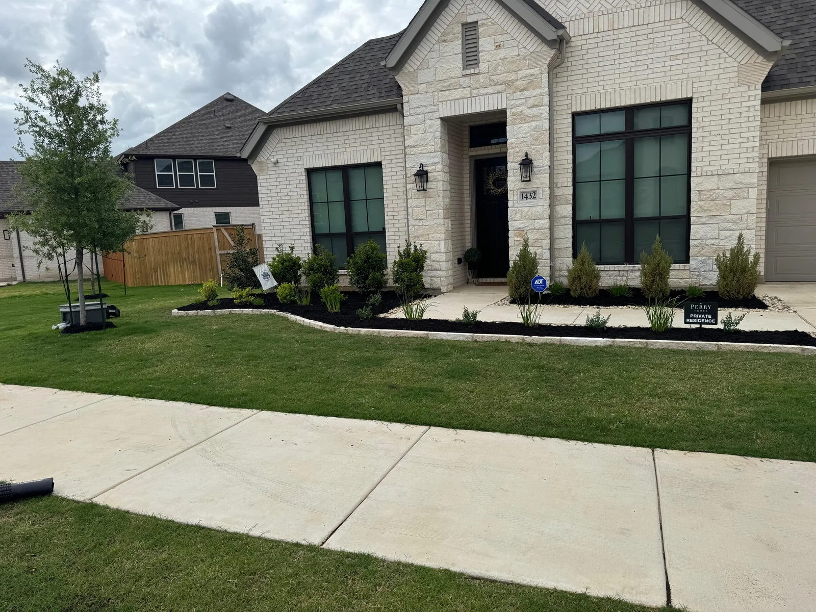 A white stone house with mulched front beds, young shrubs and a new tree.