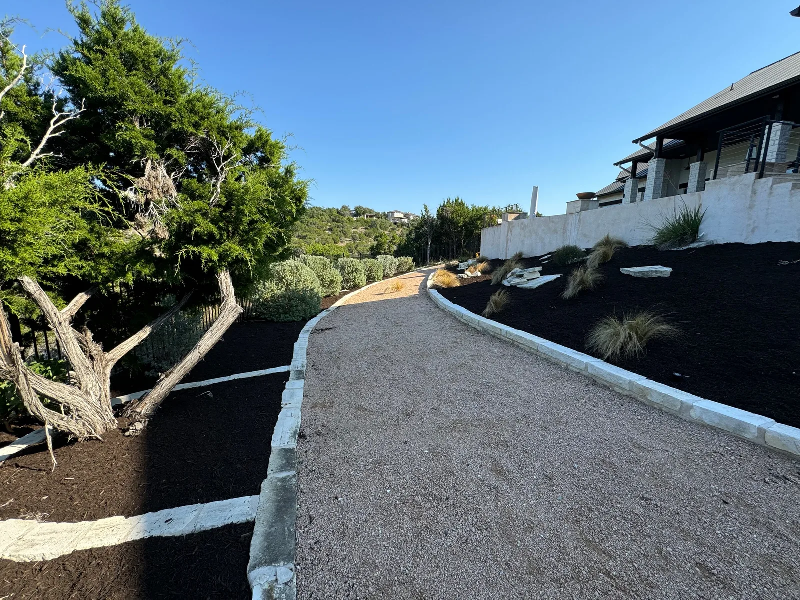 A curving gravel path between mulched planting beds with white stone edging.