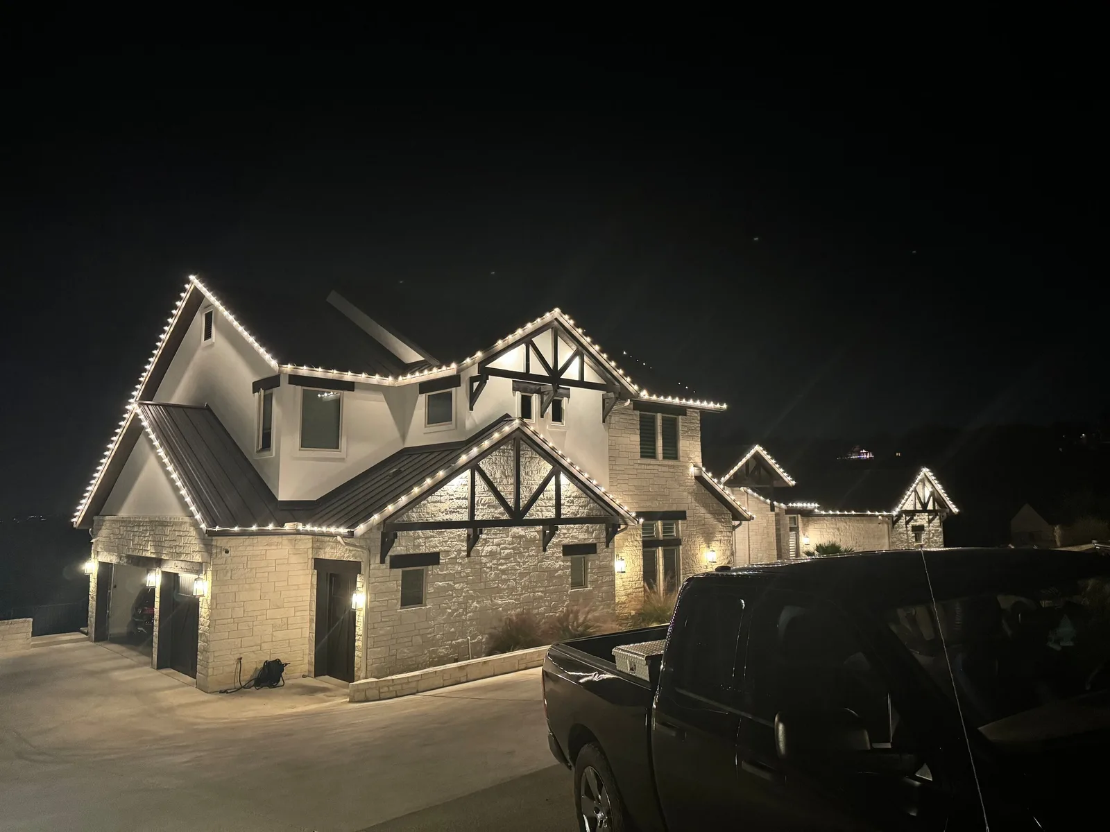 Warm white holiday lights trace the roofline of a stone house at night.
