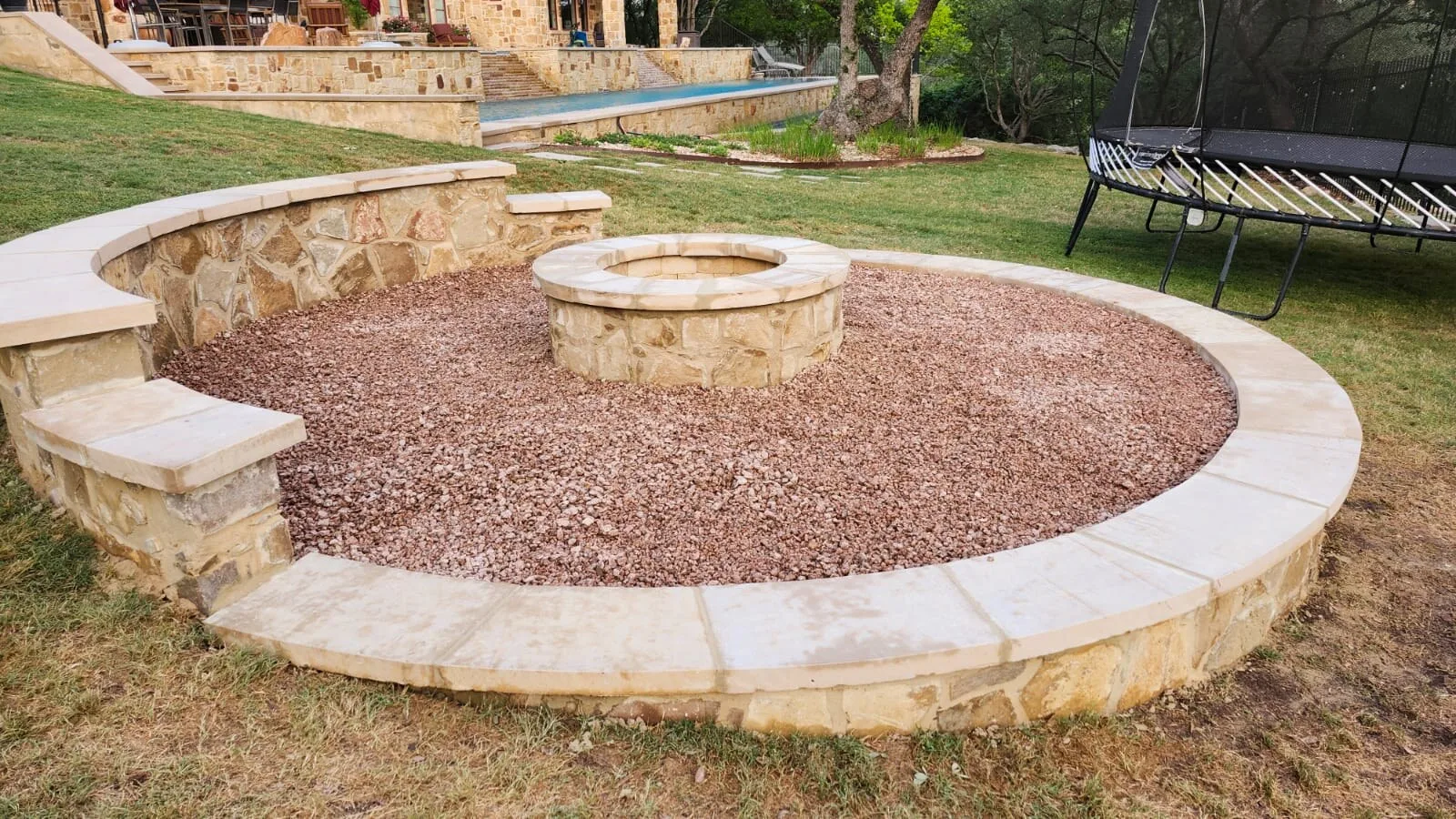 A circular stone fire pit with a gravel seating area and curved stone benches.